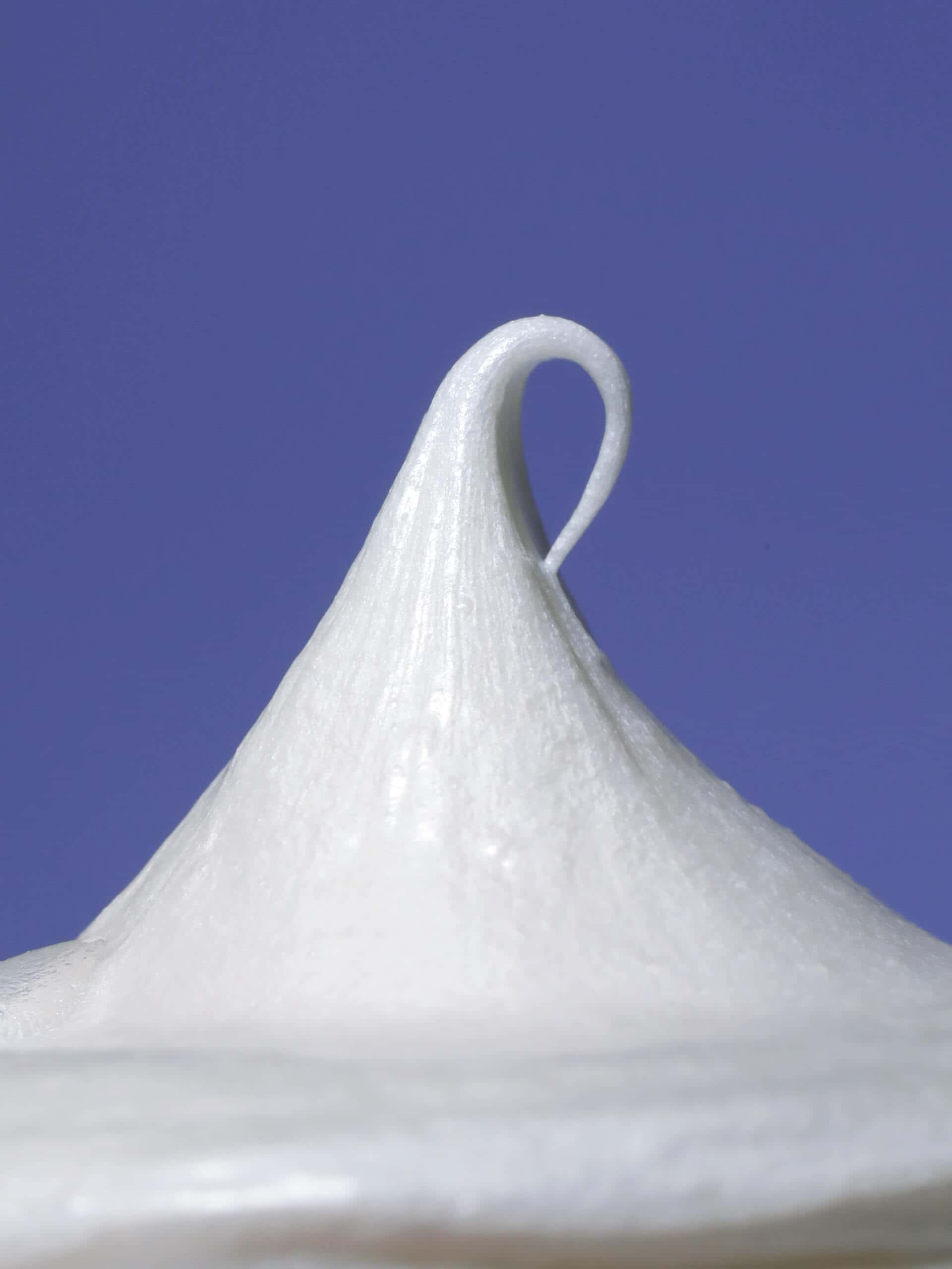 A peaked swirl of white shave cream stands against a solid blue background, showcasing its smooth texture.