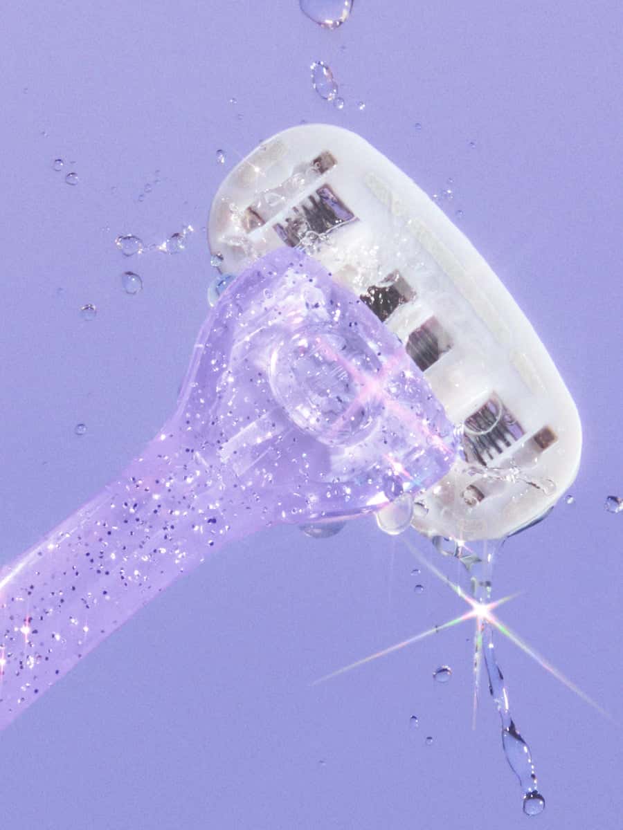 Glittery purple razor with water droplets mid-air, highlighting its textured handle and multi-blade head.