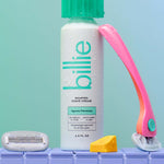 A "billie" shaving cream bottle with a pink razor, cartridge, and soap on a tiled surface.
