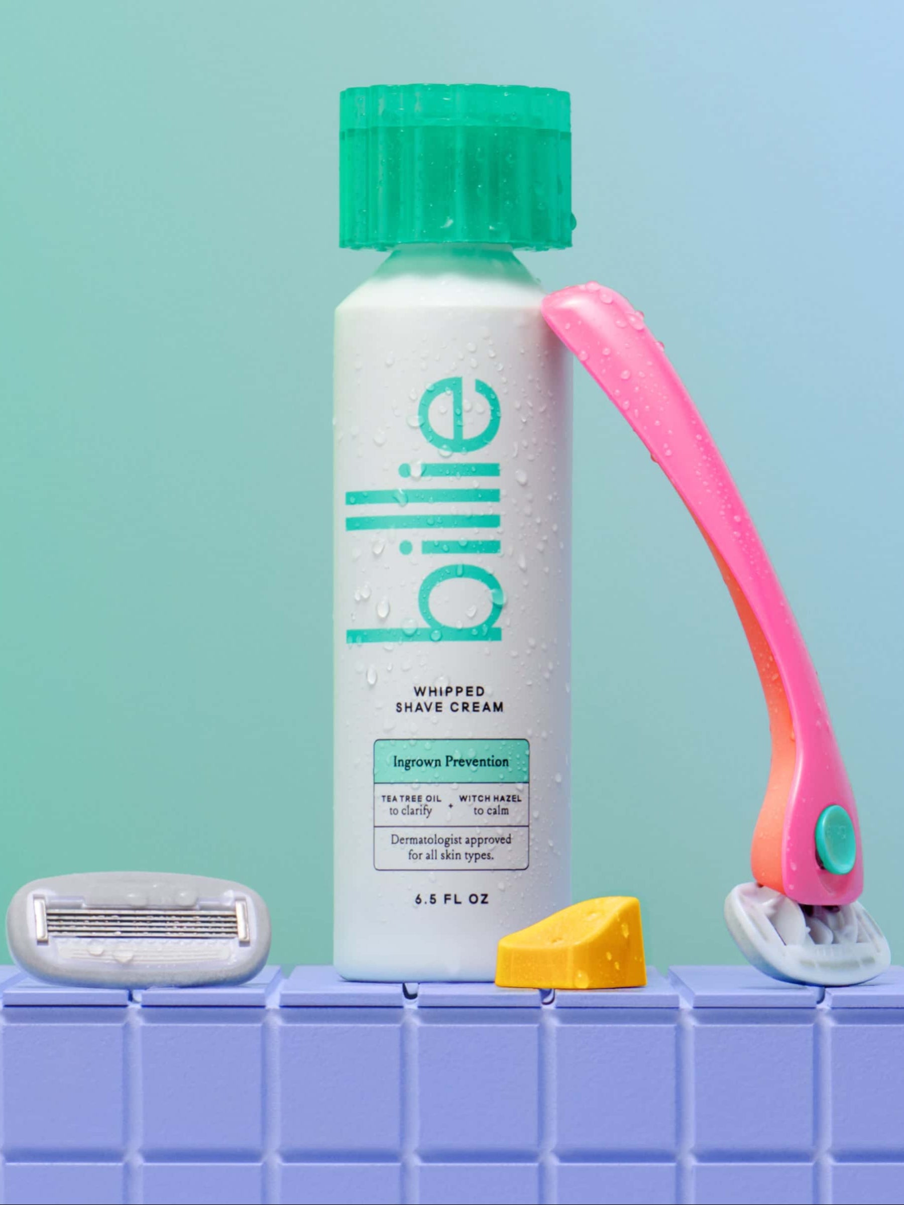 A "billie" shaving cream bottle with a pink razor, cartridge, and soap on a tiled surface.