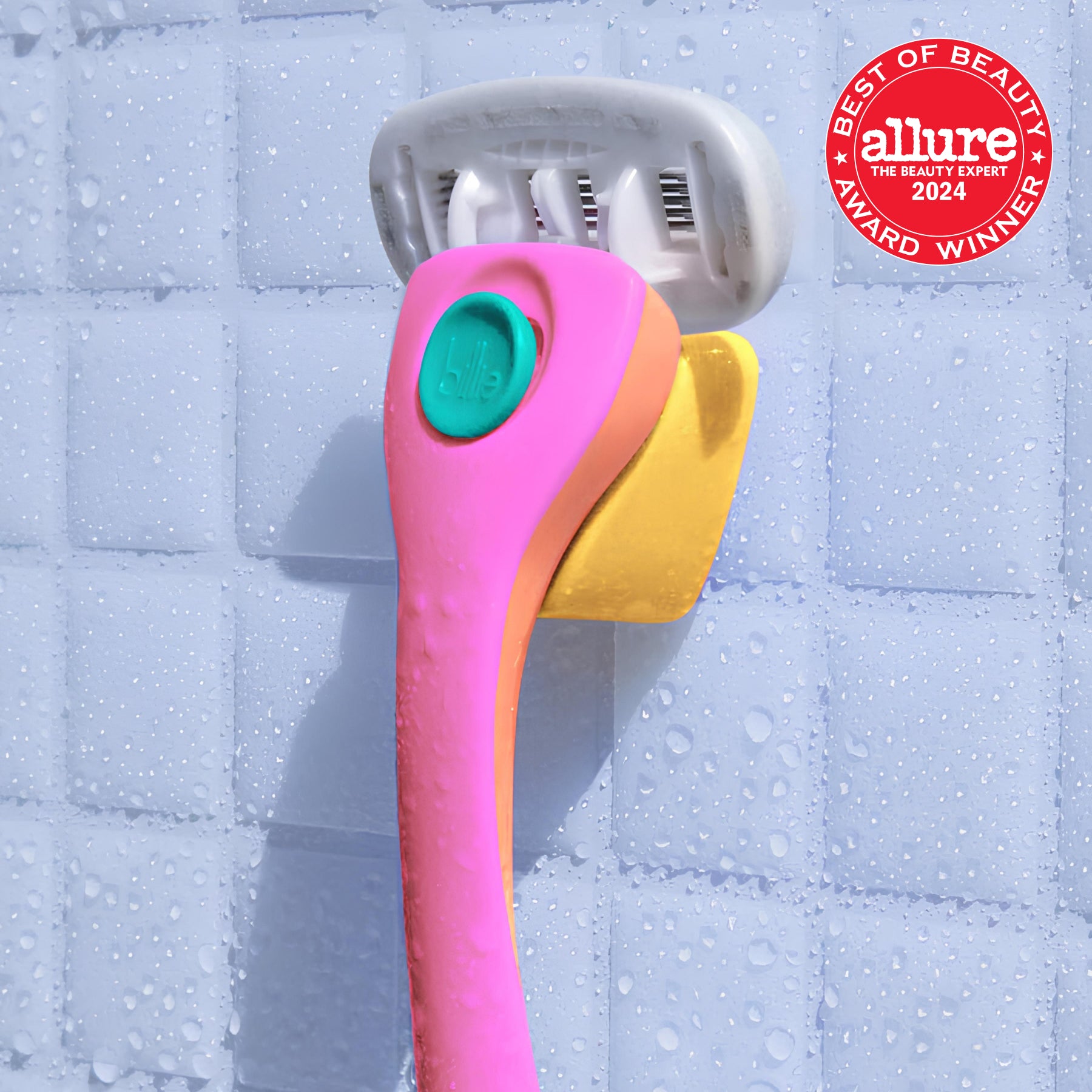 A colourful "billie" razor with pink handle on yellow holder, set against a tiled, wet shower wall.