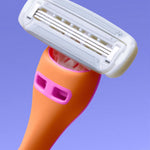A brightly colored razor with an orange handle and pink accents features a multi-blade head, positioned against a light purple background.