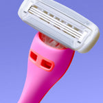 A pink razor with a white multi-blade head is angled upward against a smooth, gradient blue background.