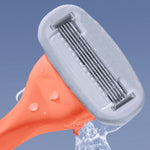 An orange razor with multiple blades is held tilted, with water splashing against the blades, set against a solid blue background.