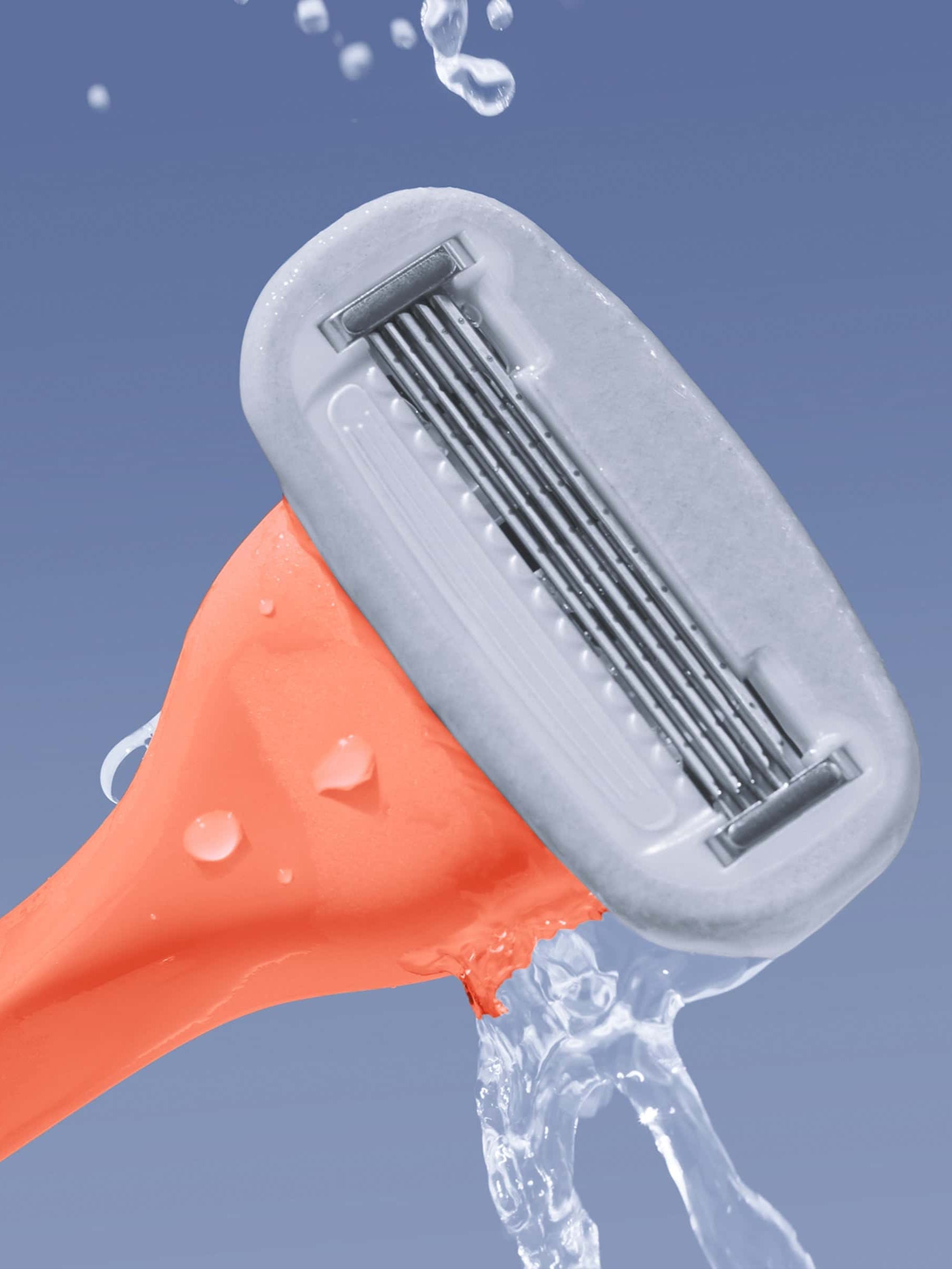 An orange razor with multiple blades is held tilted, with water splashing against the blades, set against a solid blue background.
