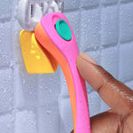 A colorful razor with a pink handle is being hung on a yellow hook, attached to a tiled bathroom wall wet with water droplets.