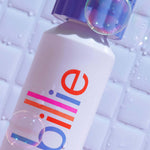 A "billie" shave cream can with blue cap, colourful branding, and soap bubbles on a tiled background.