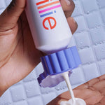 A hand dispenses shave cream from a white "billie" bottle onto another palm, against a wet tiled background.