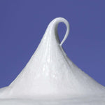 A peaked swirl of white shave cream stands against a solid blue background, showcasing its smooth texture.