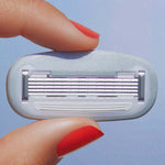 Red-polished fingers hold a multi-blade razor cartridge against a plain light blue background.