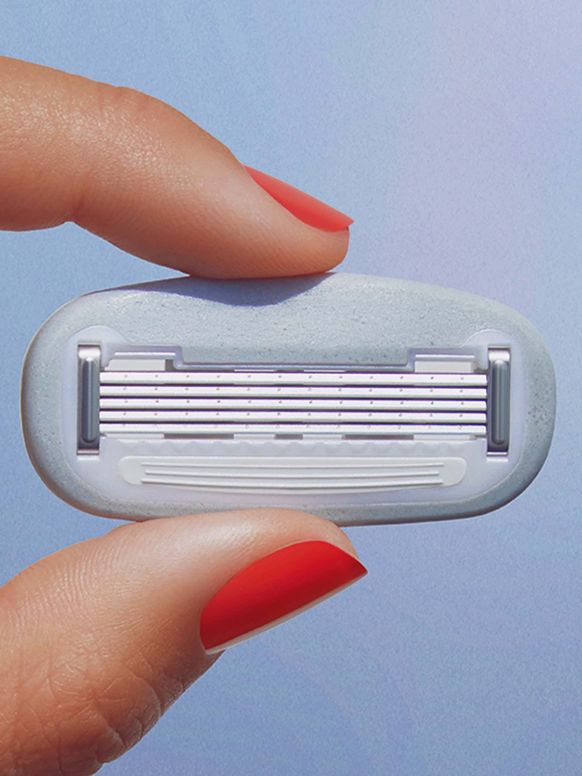Red-polished fingers hold a multi-blade razor cartridge against a plain light blue background.