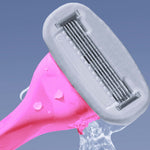 A pink multi-blade razor being rinsed, with water droplets on it and in the air, against a blue background.