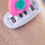 Close-up of pink-orange razor gliding over skin, showing blades and textured handle for precise grooming.