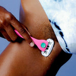 A hand shaves a wet thigh with a pink "Billie" razor; blue tie-dye clothing is partially visible.