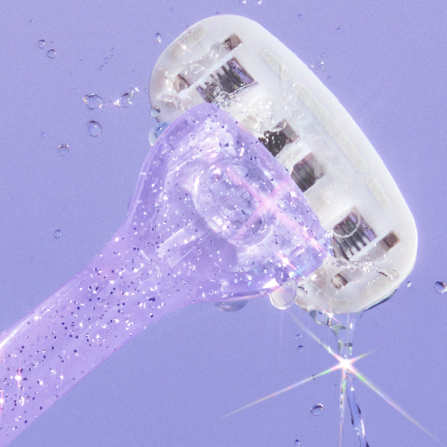 Glittery purple razor with water droplets mid-air, highlighting its textured handle and multi-blade head.