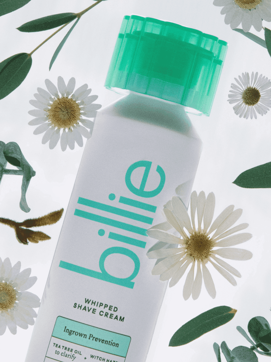 Billie shave cream with green cap, daisies, and leaves; features ingrown prevention, tea tree oil, and witch hazel.