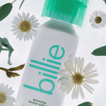 Billie shave cream with green cap, daisies, and leaves; features ingrown prevention, tea tree oil, and witch hazel.