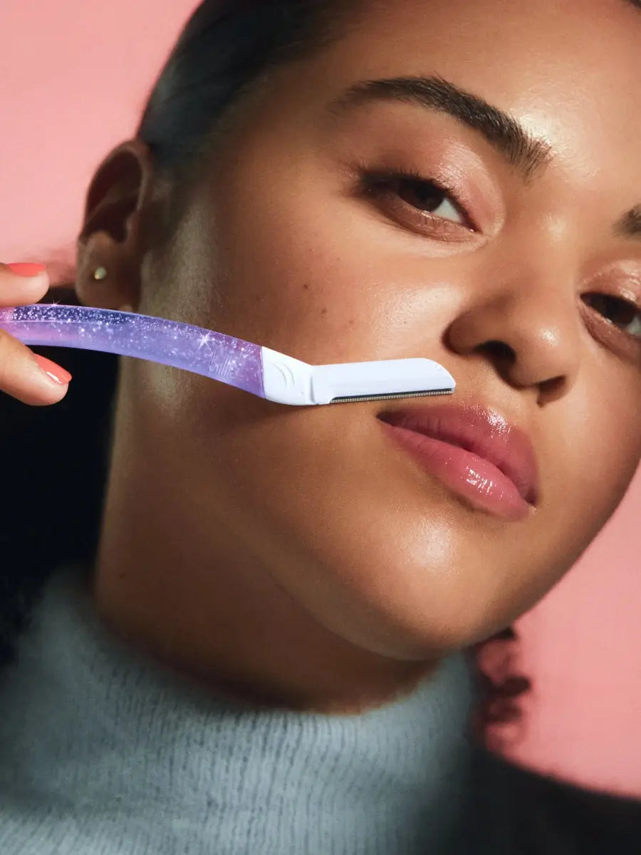 Close-up of purple facial razor marked "smile" used on cheek, with pink background and grey top.